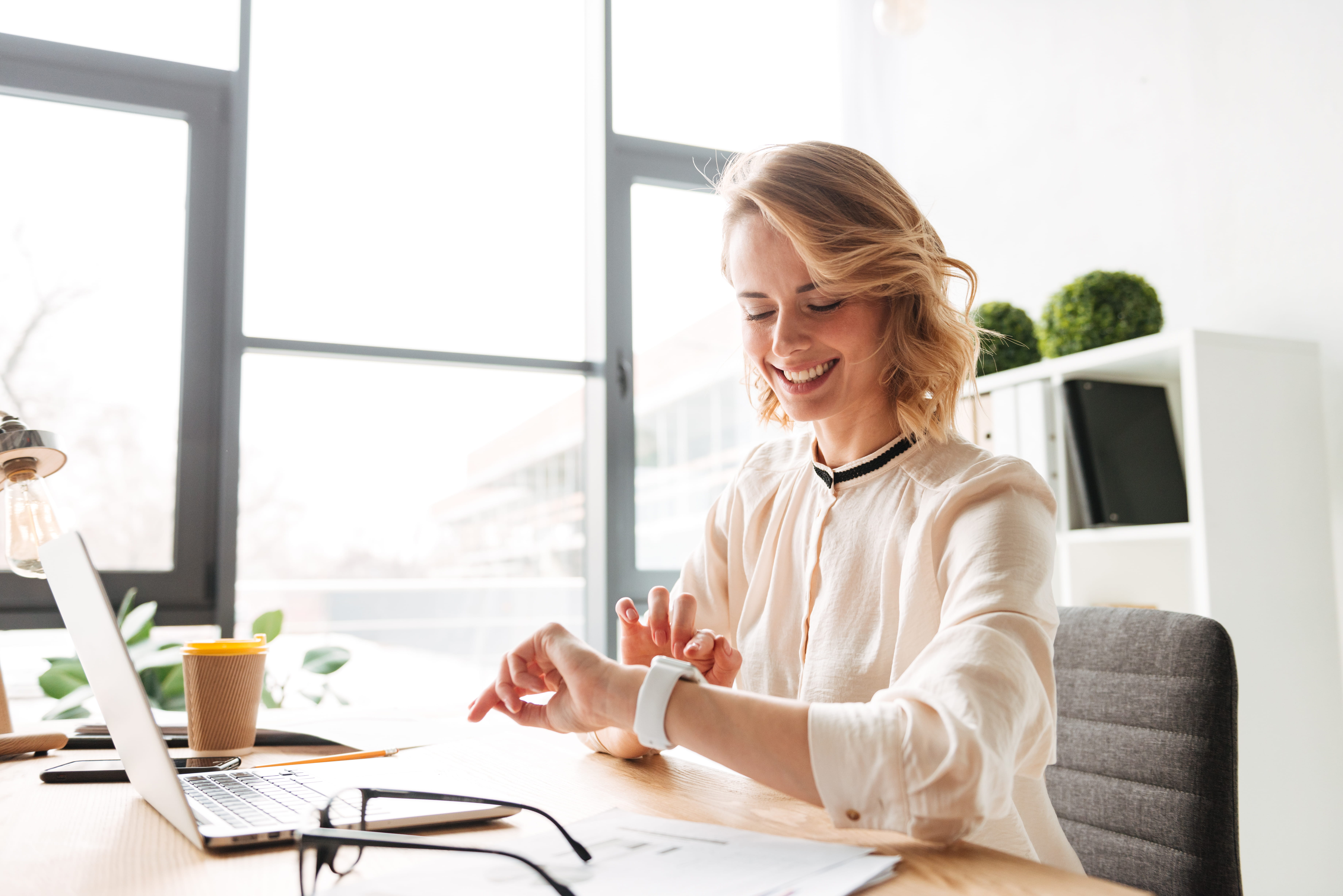 Smiling person sitting at a desk holding a notebook in colorful office.